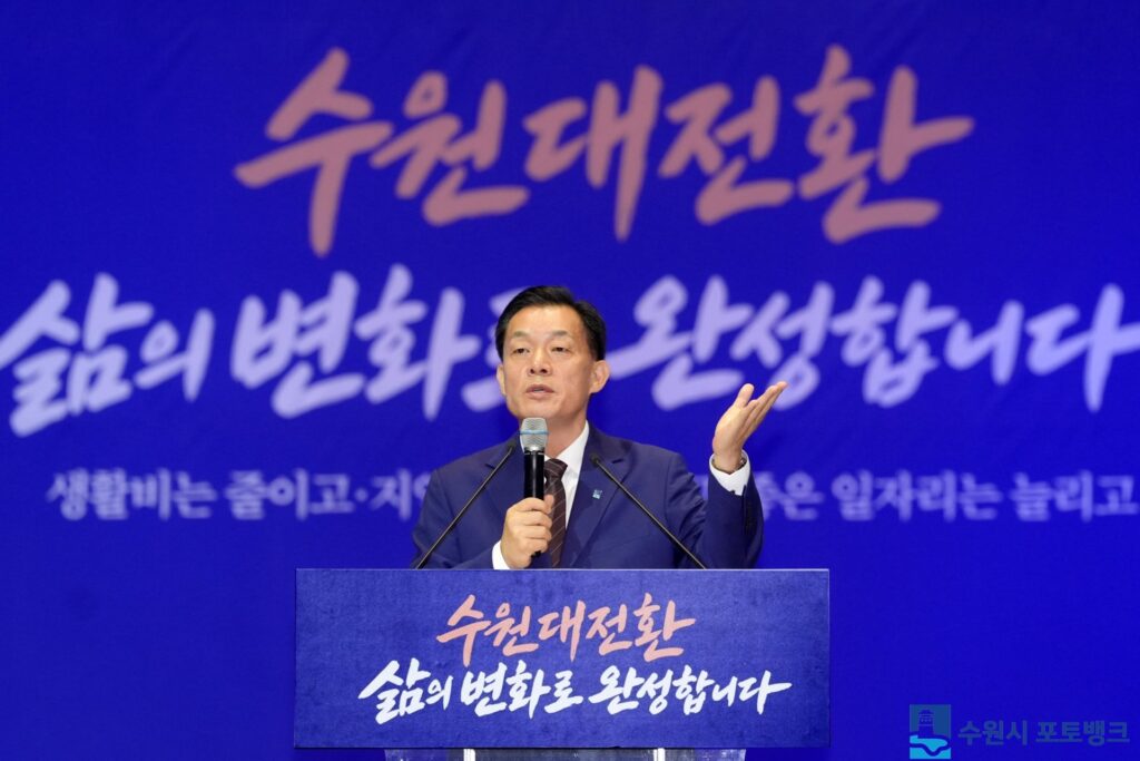 수원대전환 삶의 변화로 완성합니다 문구가 적힌 연단에서 마이크를 들고 발표하는 이재준 수원시장